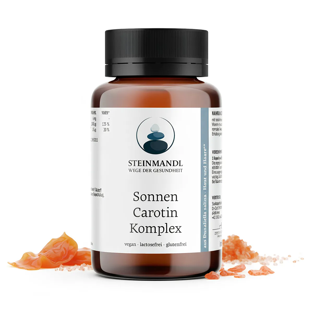 Eine braune Flasche Sonnen Carotin Komplex steht neben orangefarbenen Kapseln und Granulat auf einem weißen Hintergrund. Das Etikett hebt hervor, dass das Ergänzungsmittel vegan, laktosefrei und glutenfrei ist.